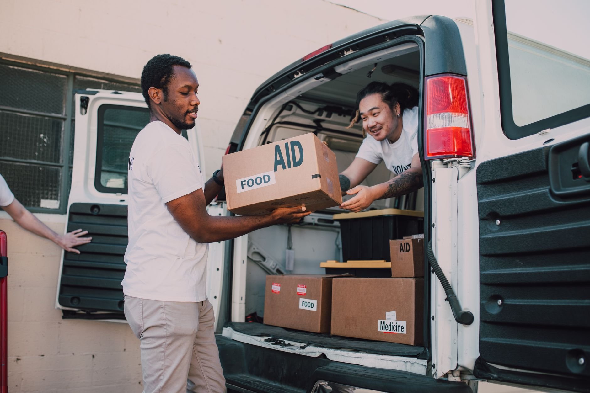 Two volunteers loading boxes labeled 'aid' into a van for community food donation drive.